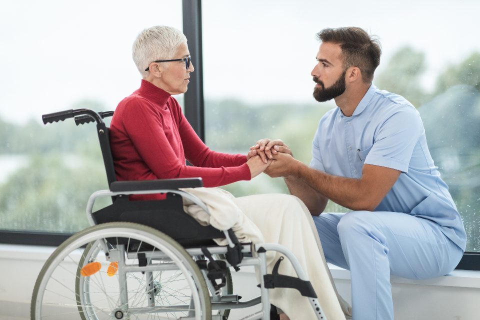 A caregiver holding hands with a senior woman in a wheelchair
