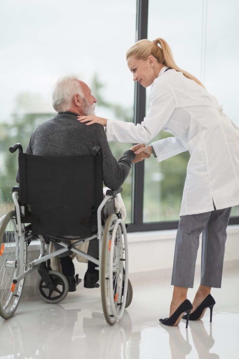A caregiver assisting a senior man in a wheelchair by a bright window
